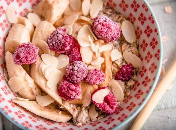 Bowl of Oats Soaked overnight with frozen raspberries, banana and flaked almonds.