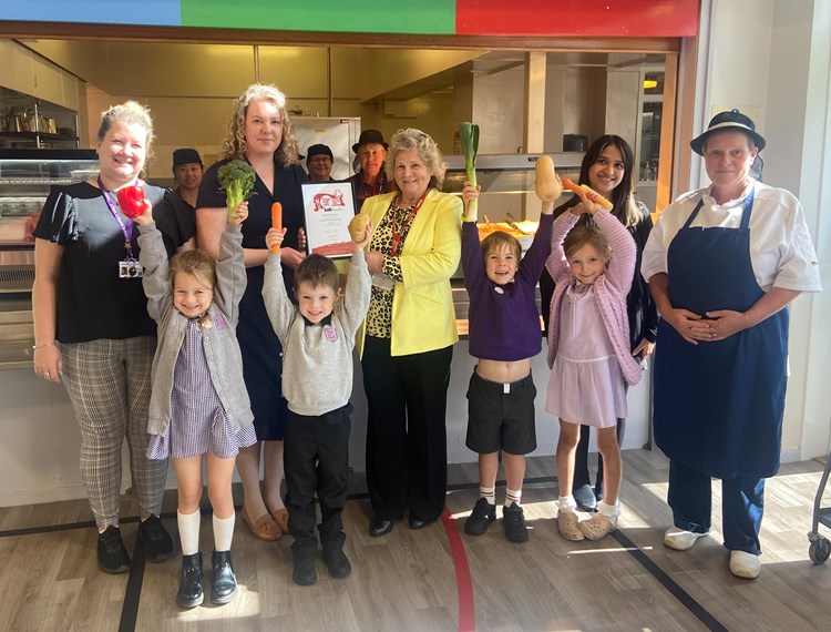 Councillor Dianne Alexander receives the Food for Life Served Here Bronze award from Lucy MacLellan at Lasswade Primary School, joined by school and council staff and P1 and P2 pupils